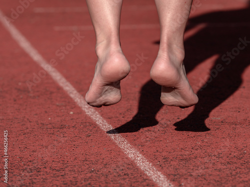 Middle aged barefoot woman warm up legs on stadium run track.
