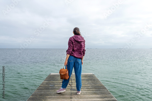 Girl with a backpack, looks at the sea, on a wooden pier. Freedom. Trips. © vallerato