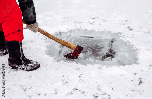 Woman person making ice hole with an ax in the winter for ice bath and taking water.