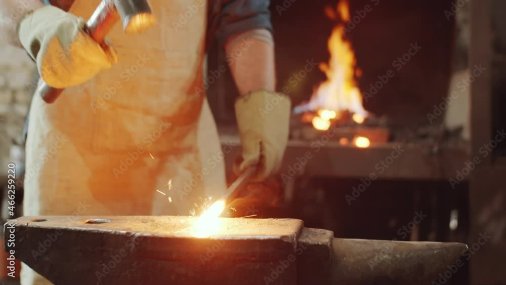 Midsection shot of unrecognizable blacksmith in apron and gloves taking off hot metal rod from fire in forge and hammering it on anvil Midsection shot of unrecognizable blacksmith in apron and gloves taking off hot metal rod from fire in forge and hammering it on anvil