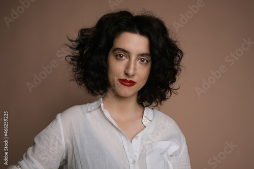 Portrait of young woman with curly hair posing over brown background. Isolated.