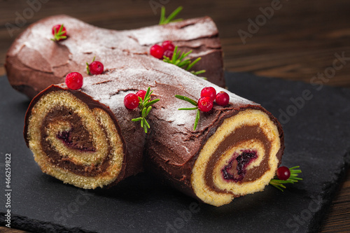 Traditional homemade Christmas cake. Yule log or Buche de Noel. Sponge cake with chocolate cream, ganache, decorated with cranberries Dark wooden background.