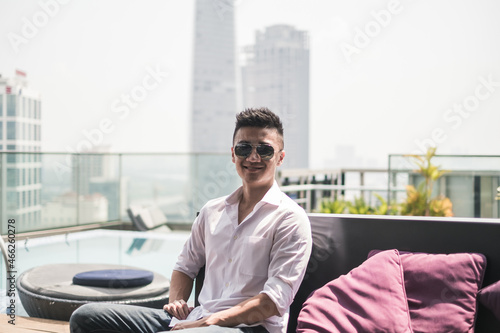 Handsome young Asian man sitting on the rooftop near the swimming pool. Chinese guy, millennials life, lifestyle in the big city, Modern Asia