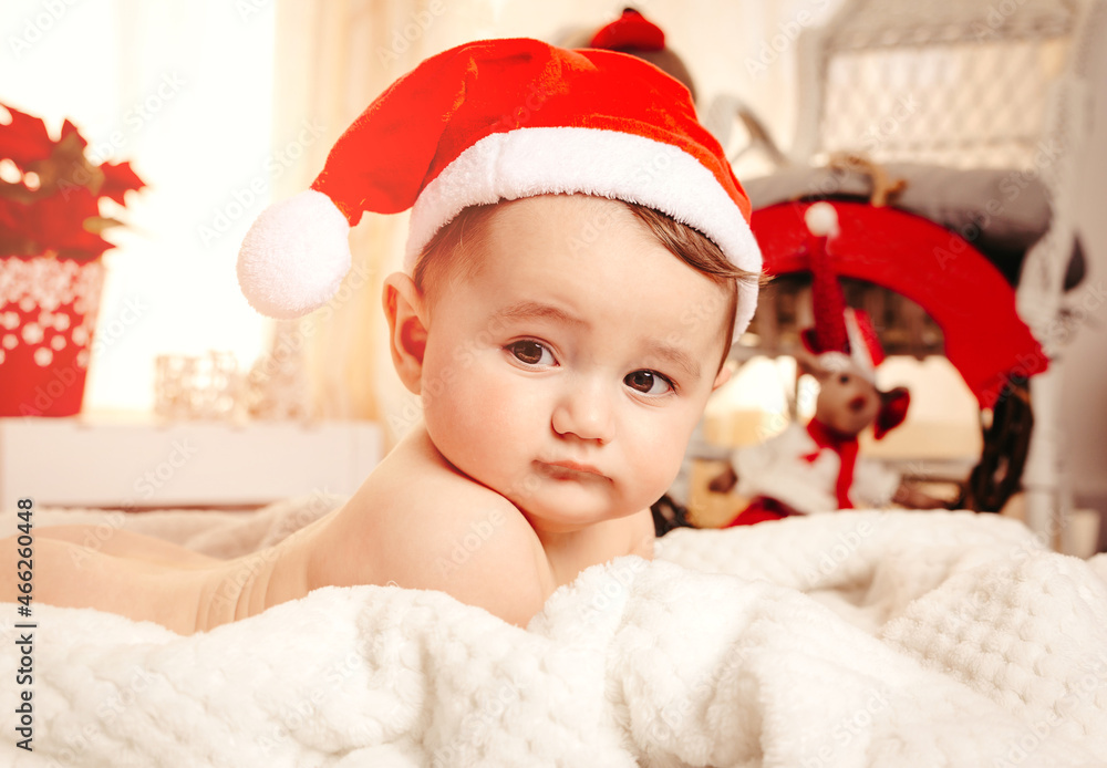 Sweet baby Christmas with santa hat and ornaments on the background. Cute little child on a cozy blanket. Merry Xmas and winter holiday season concept Sweet baby Christmas with santa hat and ornaments on the background. Cute little child on a cozy blanket. Merry Xmas and winter holiday season concept