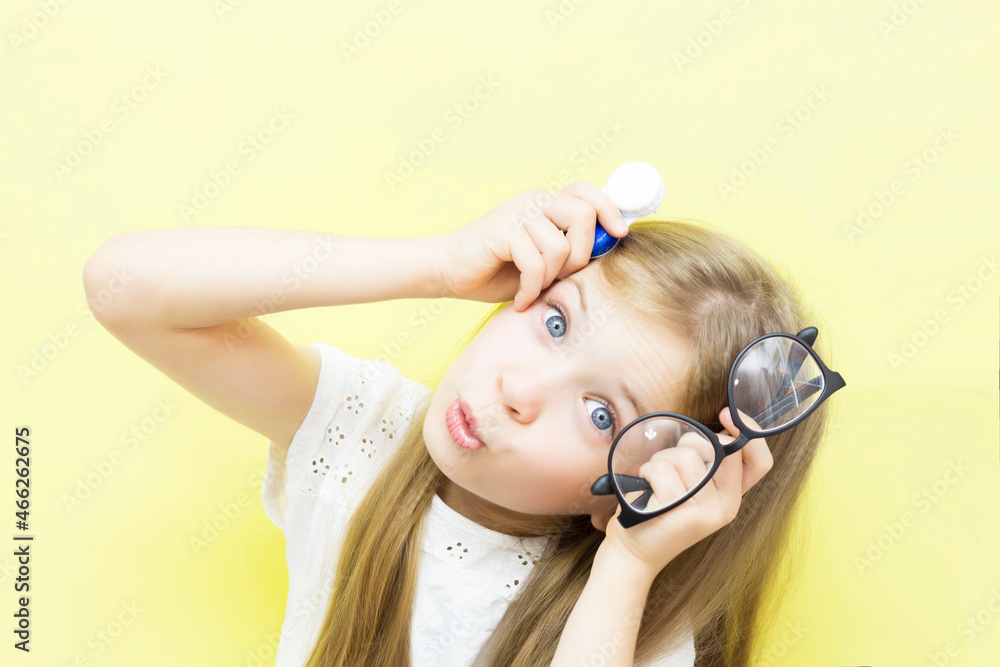 Εκτύπωση καμβά A beautiful baby with long hair holds a container with lenses and glasses in her hands