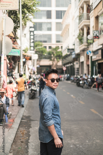 Portrait of asian young handsome man in denim shirt and sunglasses standing on the street and looking at camera with copy space. Chinese people