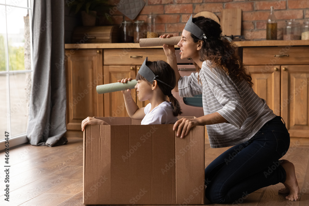 Happy creative mother and active daughter girl playing pirates ship at home, sailing carton box boat, looking forward through toy paper spyglasses, enjoying home activities. Family role game - obrazy, fototapety, plakaty 