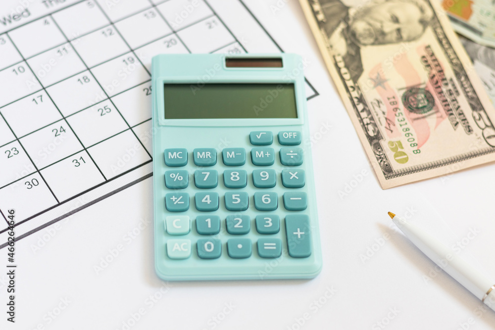 Mini calculator, blank calendar, pen and US dollars, 50 and 100. American cash, savings, taxes, benefit, income, money, finance. Top view, flat lay. Mini calculator, blank calendar, pen and US dollars, 50 and 100. American cash, savings, taxes, benefit, income, money, finance. Top view, flat lay.