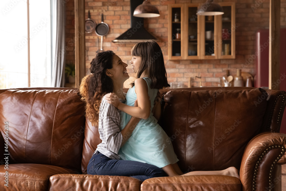 Happy laughing mom cuddling daughter girl on couch at home, playing with kid, hugging child with love, tenderness, care, enjoying leisure time, activity together. Motherhood, mother kid bonding Happy laughing mom cuddling daughter girl on couch at home, playing with kid, hugging child with love, tenderness, care, enjoying leisure time, activity together. Motherhood, mother kid bonding