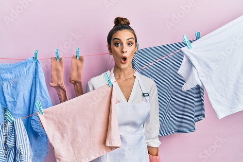 Beautiful brunette young woman washing clothes at clothesline afraid and shocked with surprise expression, fear and excited face.