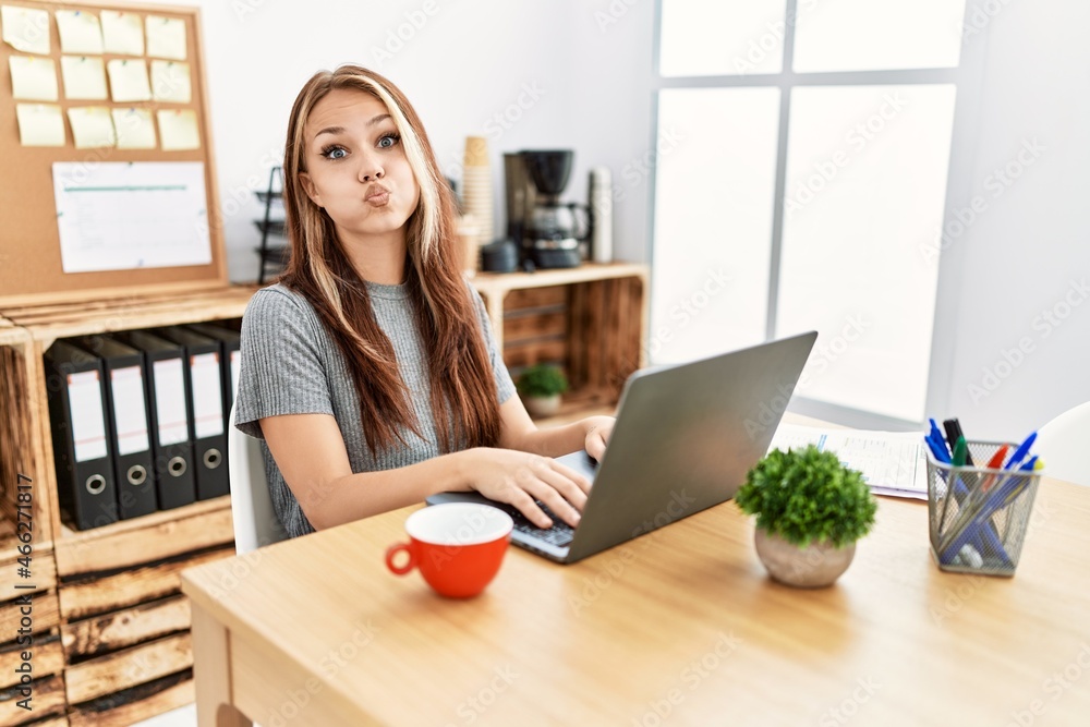 Young brunette woman working at the office with laptop puffing cheeks with funny face. mouth inflated with air, crazy expression. Young brunette woman working at the office with laptop puffing cheeks with funny face. mouth inflated with air, crazy expression.