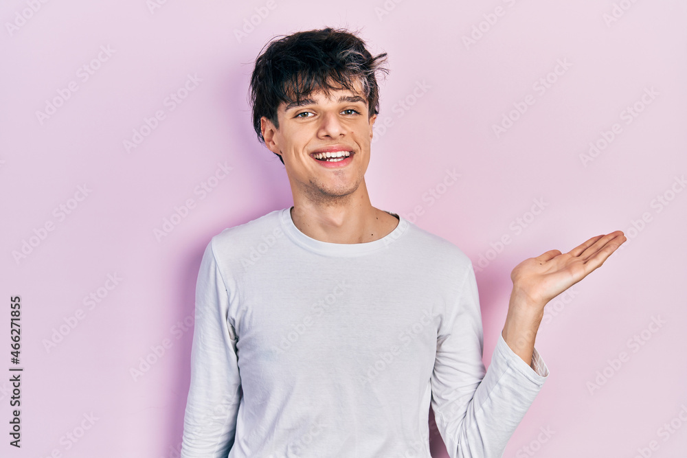 Handsome hipster young man wearing casual white shirt smiling cheerful presenting and pointing with palm of hand looking at the camera. Handsome hipster young man wearing casual white shirt smiling cheerful presenting and pointing with palm of hand looking at the camera.