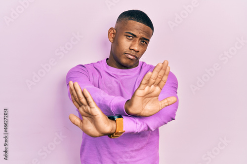 Young black man wearing casual pink sweater rejection expression crossing arms and palms doing negative sign, angry face