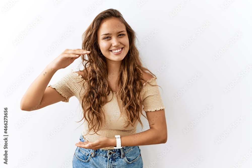 Beautiful hispanic woman standing over isolated while background gesturing with hands showing big and large size sign, measure symbol. smiling looking at the camera. measuring concept. Beautiful hispanic woman standing over isolated while background gesturing with hands showing big and large size sign, measure symbol. smiling looking at the camera. measuring concept.