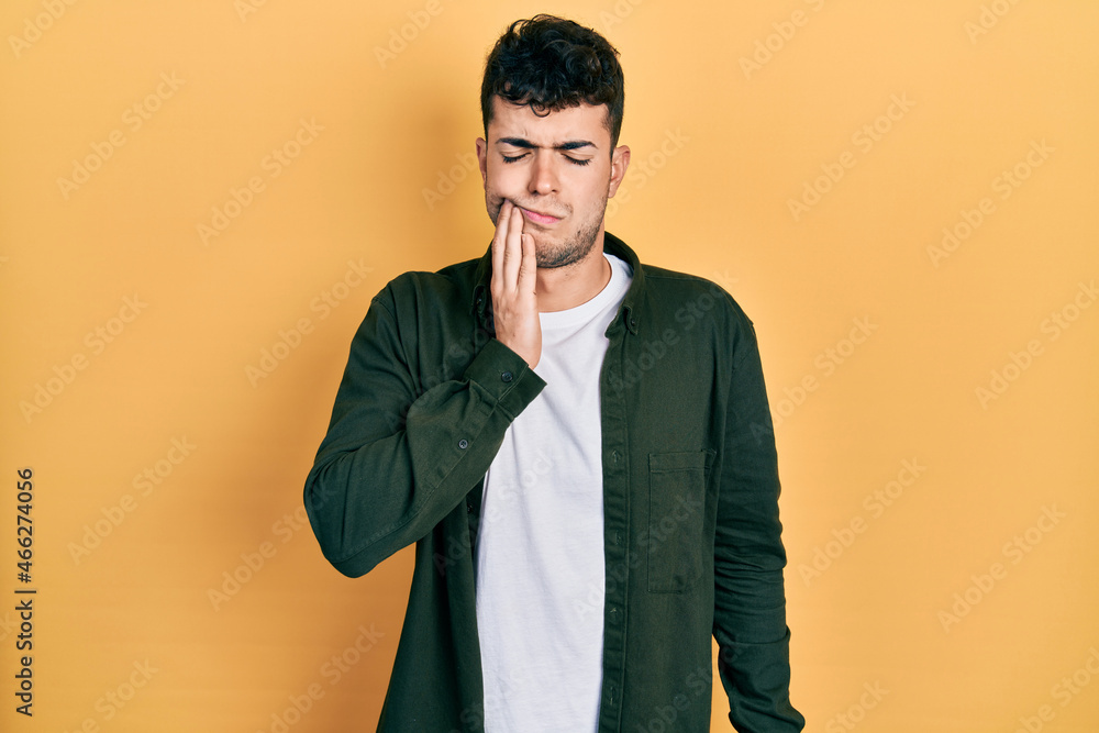 Young hispanic man wearing casual clothes touching mouth with hand with painful expression because of toothache or dental illness on teeth. dentist Young hispanic man wearing casual clothes touching mouth with hand with painful expression because of toothache or dental illness on teeth. dentist