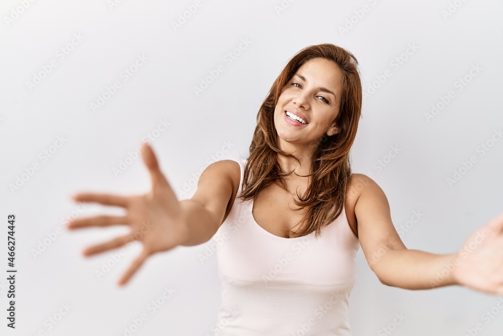 Middle age hispanic woman standing over isolated background looking at the camera smiling with open arms for hug. cheerful expression embracing happiness. Middle age hispanic woman standing over isolated background looking at the camera smiling with open arms for hug. cheerful expression embracing happiness.