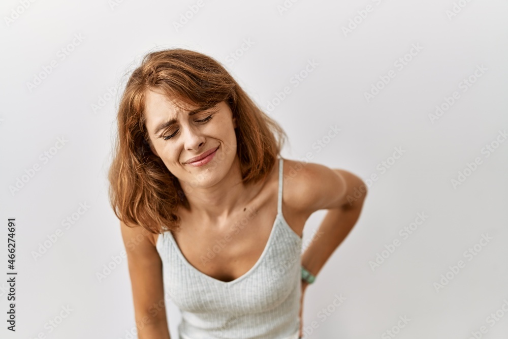 Beautiful caucasian woman standing over isolated background suffering of backache, touching back with hand, muscular pain Beautiful caucasian woman standing over isolated background suffering of backache, touching back with hand, muscular pain