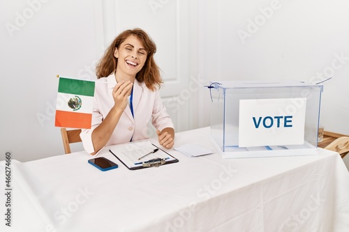 Beautiful caucasian woman at political campaign election holding mexico flag looking positive and happy standing and smiling with a confident smile showing teeth