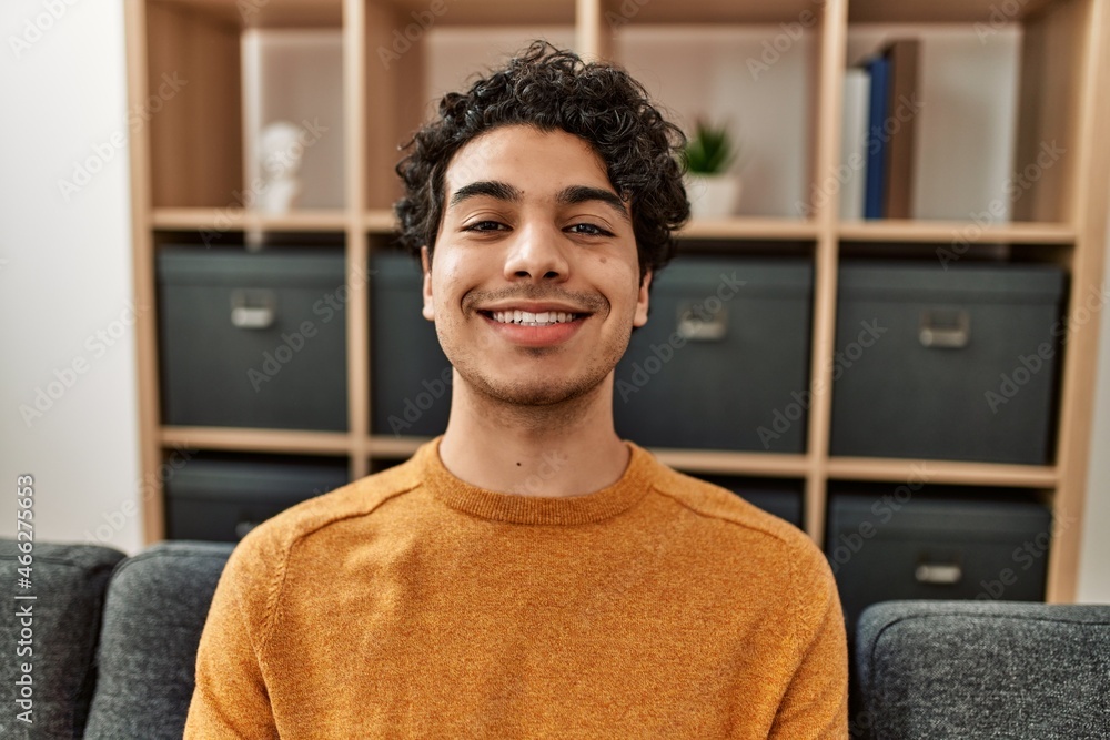 Young hispanic man smiling happy sitting on the sofa at home. Young hispanic man smiling happy sitting on the sofa at home.