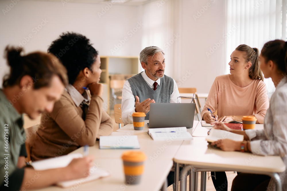 Mature professor uses laptop while talking to group of students in classroom. Mature professor uses laptop while talking to group of students in classroom.