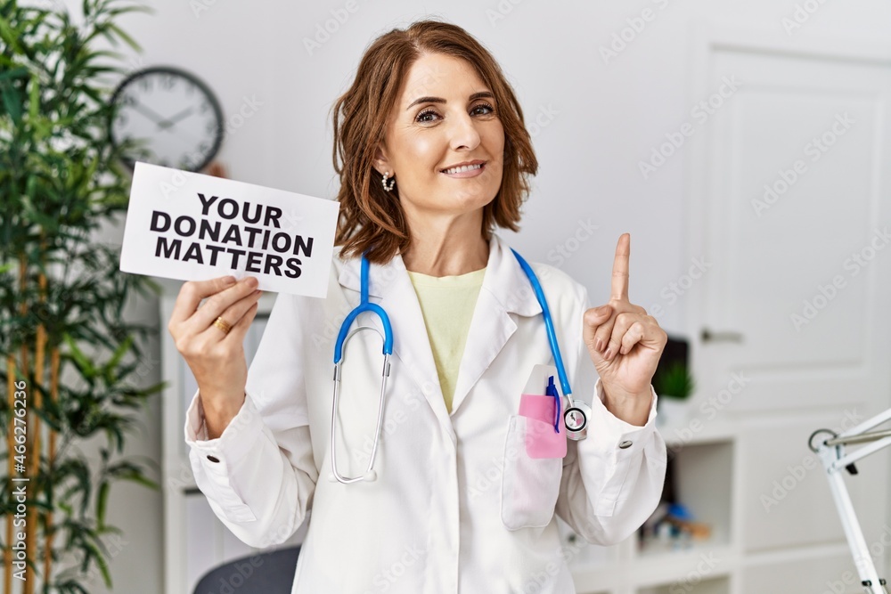Middle age doctor woman holding your donation matters at the clinic surprised with an idea or question pointing finger with happy face, number one Middle age doctor woman holding your donation matters at the clinic surprised with an idea or question pointing finger with happy face, number one