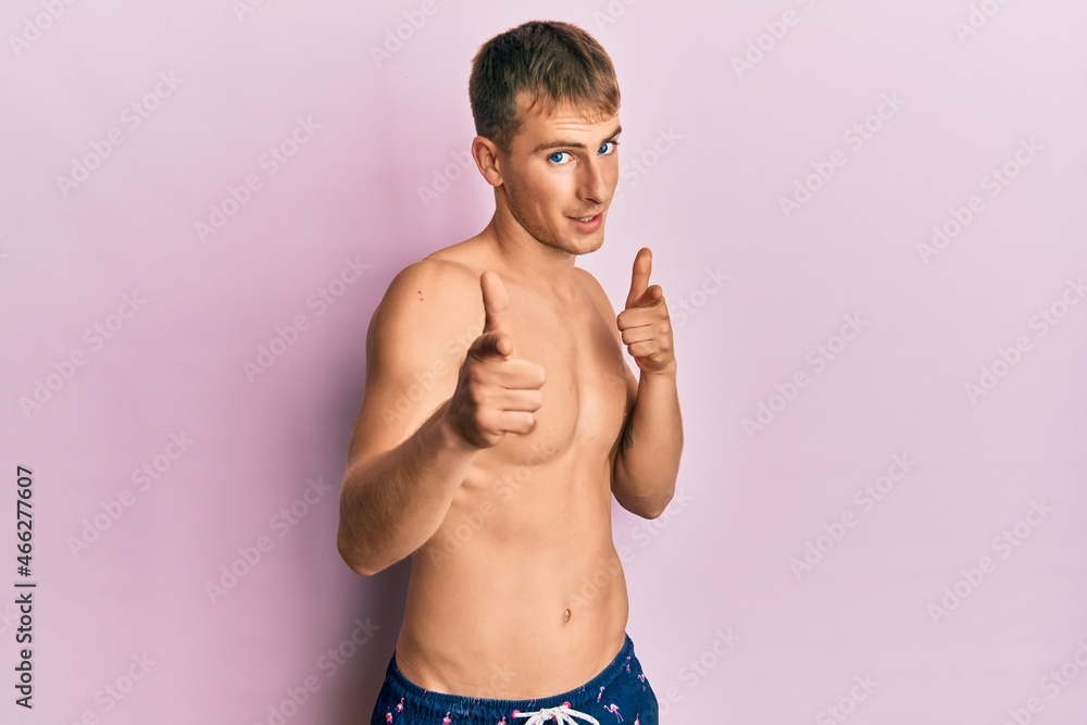 Young caucasian man wearing swimwear pointing fingers to camera with happy and funny face. good energy and vibes.