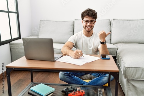 Hispanic man doing papers at home pointing to the back behind with hand and thumbs up, smiling confident