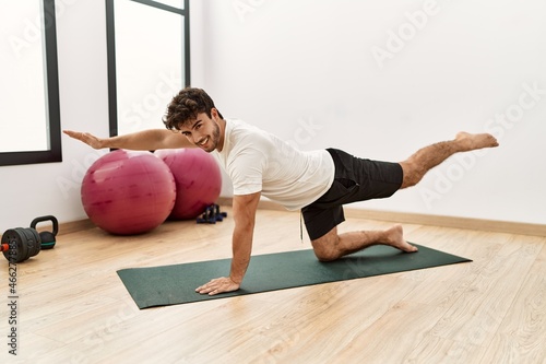 Young hispanic man smiling confident stretching at sport center