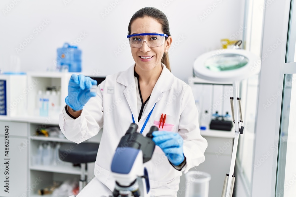 Young hispanic woman wearing scientist uniform using microscope at laboratory Young hispanic woman wearing scientist uniform using microscope at laboratory