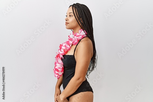 Young african american woman wearing swimsuit and hawaiian lei looking to side, relax profile pose with natural face and confident smile.
