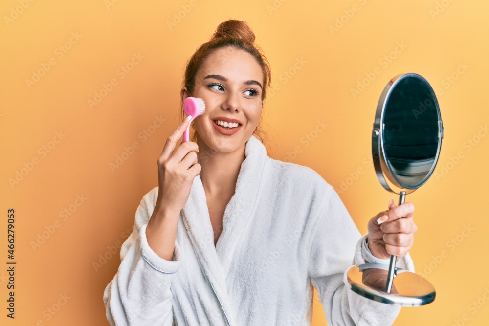 Young blonde woman wearing robe holding makeup remover brush smiling with a happy and cool smile on face. showing teeth. Young blonde woman wearing robe holding makeup remover brush smiling with a happy and cool smile on face. showing teeth.