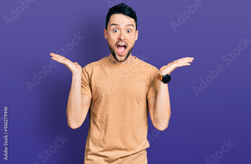 Hispanic man with beard wearing casual t shirt celebrating crazy and amazed for success with arms raised and open eyes screaming excited. winner concept