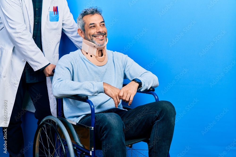 Handsome middle age man with grey hair on wheelchair wearing cervical collar looking away to side with smile on face, natural expression. laughing confident. Handsome middle age man with grey hair on wheelchair wearing cervical collar looking away to side with smile on face, natural expression. laughing confident.