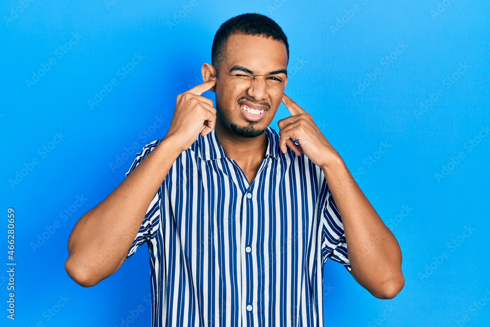 Young african american man wearing casual clothes covering ears with fingers with annoyed expression for the noise of loud music. deaf concept. Young african american man wearing casual clothes covering ears with fingers with annoyed expression for the noise of loud music. deaf concept.