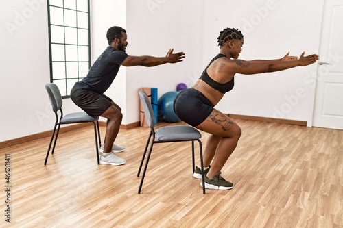 Young african american couple training using chair at sport center.