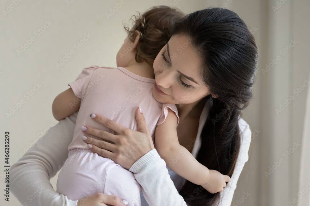 Close up beautiful loving young mother hugging cute little daughter, family enjoying tender moment at home, caring mom embracing holding adorable toddler child girl, happy motherhood concept Close up beautiful loving young mother hugging cute little daughter, family enjoying tender moment at home, caring mom embracing holding adorable toddler child girl, happy motherhood concept