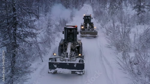 Two graders are cleaning a snow-covered forest road, the footages were taken on a quadcopter