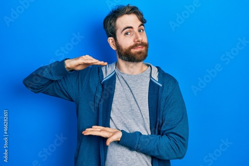 Caucasian man with beard wearing casual sweatshirt gesturing with hands showing big and large size sign, measure symbol. smiling looking at the camera. measuring concept.