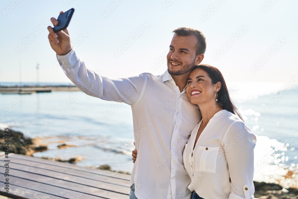 Man and woman couple hugging each other make selfie by the smartphone standing at seaside Man and woman couple hugging each other make selfie by the smartphone standing at seaside