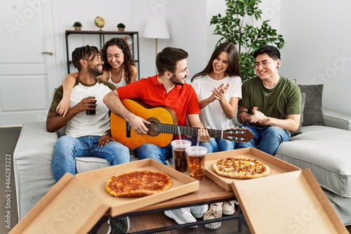 Group of young friends having party eating italian pizza and playing classical guitar at home.