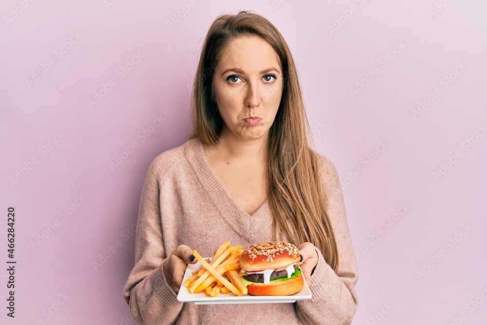 Young blonde woman eating a tasty classic burger with fries depressed and worry for distress, crying angry and afraid. sad expression. Young blonde woman eating a tasty classic burger with fries depressed and worry for distress, crying angry and afraid. sad expression.