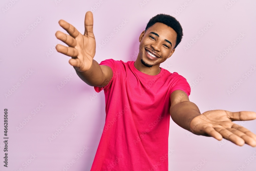 Young african american man wearing casua t shirt looking at the camera smiling with open arms for hug. cheerful expression embracing happiness. Young african american man wearing casua t shirt looking at the camera smiling with open arms for hug. cheerful expression embracing happiness.