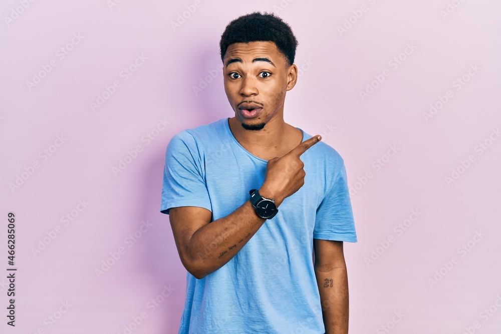 Young african american man wearing casual blue t shirt surprised pointing with finger to the side, open mouth amazed expression. Young african american man wearing casual blue t shirt surprised pointing with finger to the side, open mouth amazed expression.