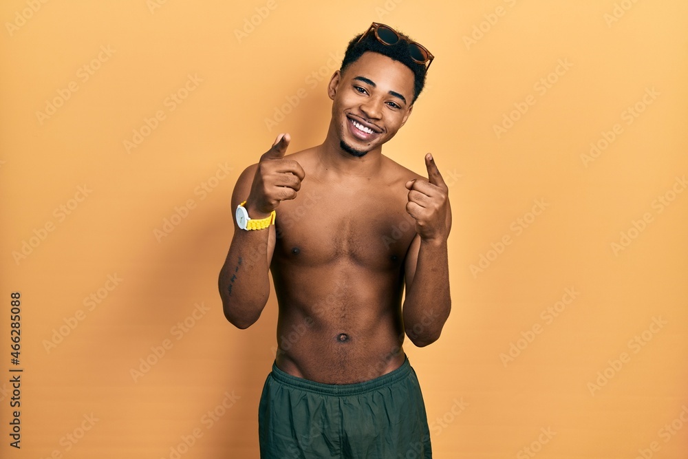 Young african american man wearing swimwear and swimmer glasses pointing fingers to camera with happy and funny face. good energy and vibes.