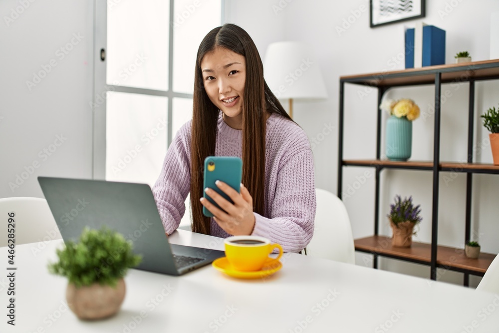 Young chinese girl using laptop and smartphone sitting on the table at home. Young chinese girl using laptop and smartphone sitting on the table at home.