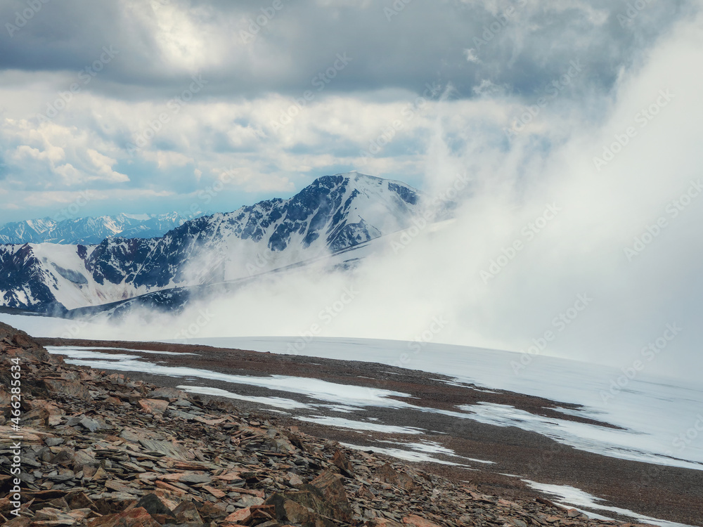 Storm on the top of a mountain. Wonderful dramatic landscape with big snowy mountain peaks above low clouds. Atmospheric large snow mountain tops in cloudy sky.