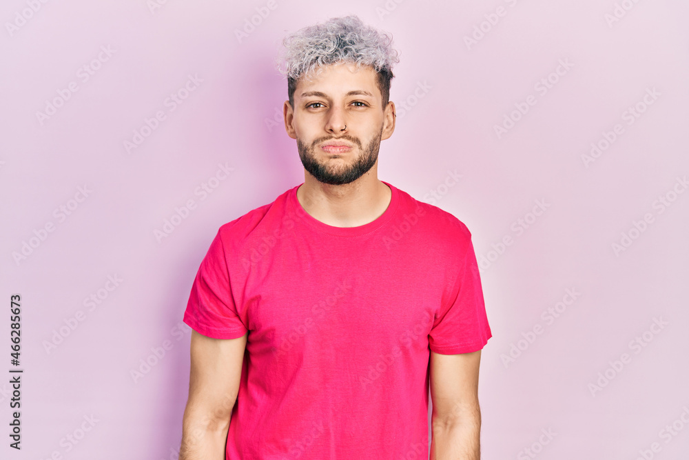 Young hispanic man with modern dyed hair wearing casual pink t shirt puffing cheeks with funny face. mouth inflated with air, crazy expression. Young hispanic man with modern dyed hair wearing casual pink t shirt puffing cheeks with funny face. mouth inflated with air, crazy expression.