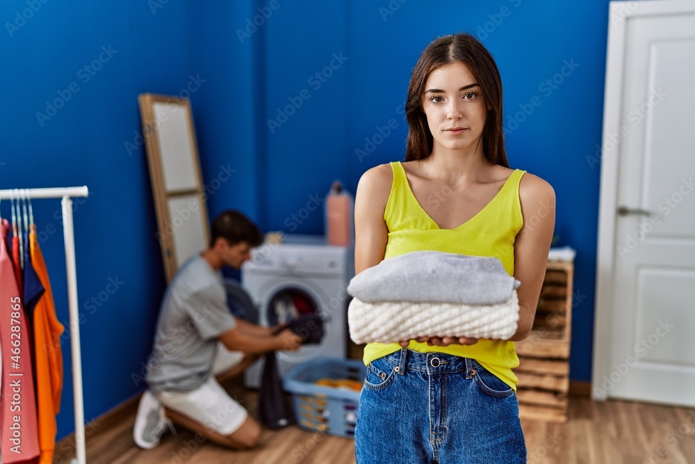 Young brunette woman holding folded laundry thinking attitude and sober expression looking self confident