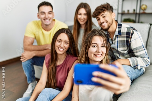 Group of young friends smiling happy make selfie by the smartphone sitting on the sofa at home.