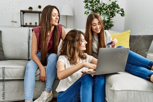 Three young hispanic woman smiling happy using laptop and credit card sitting on the sofa at home.